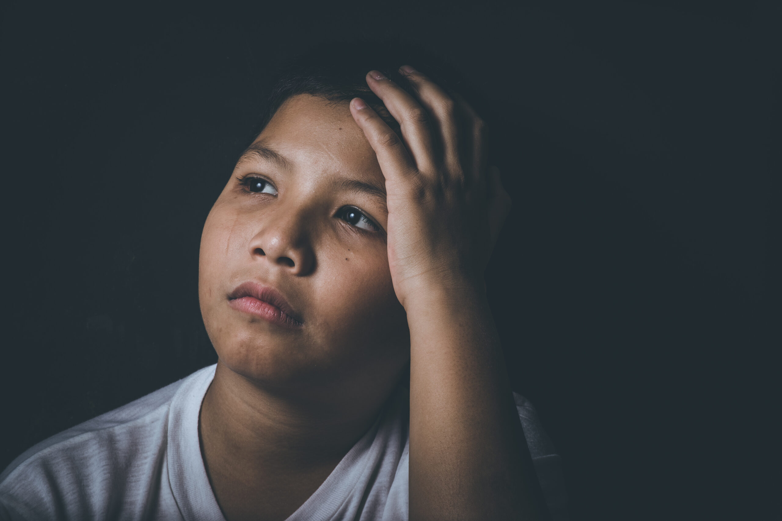 A pre-teen child looks off camera with a serious look on their face, with nothing but a shadowy, black background