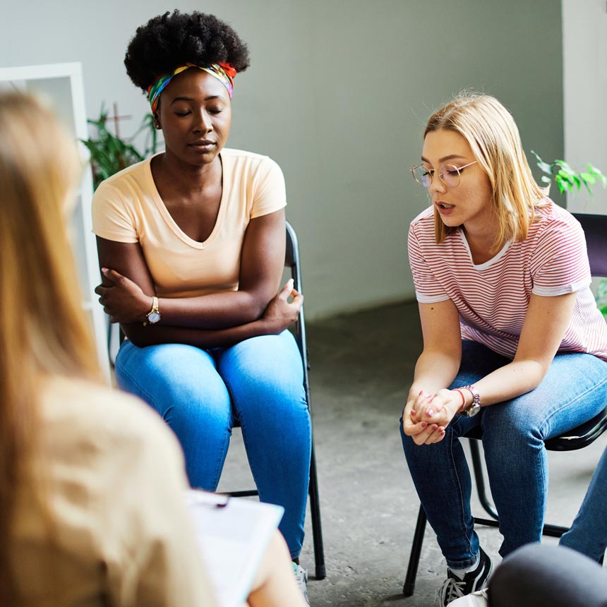 A woman sits in a group in a striped red t-shirt and shares her story with others.