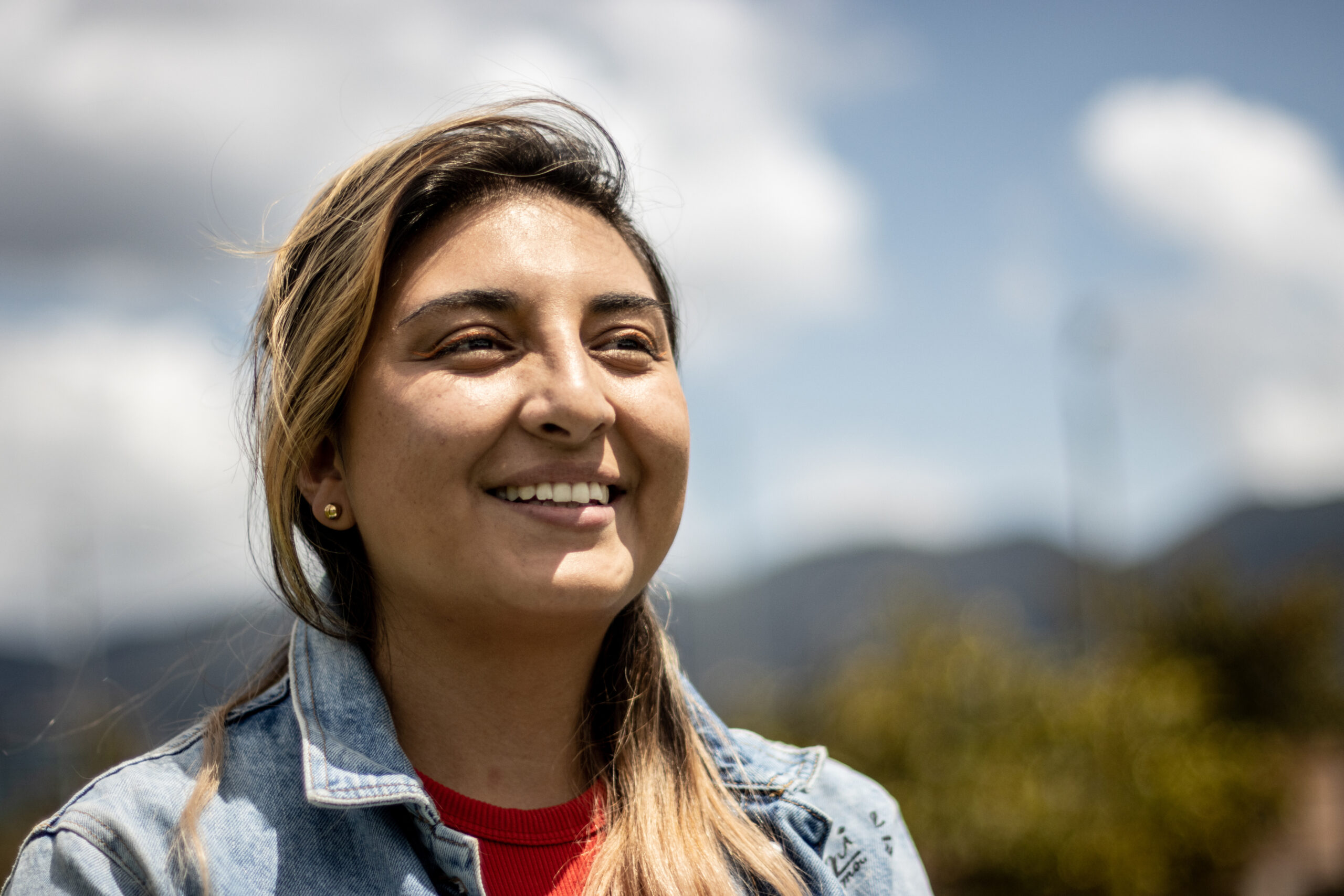 Smiling woman looking out over an outdoor scene on a sunny day.