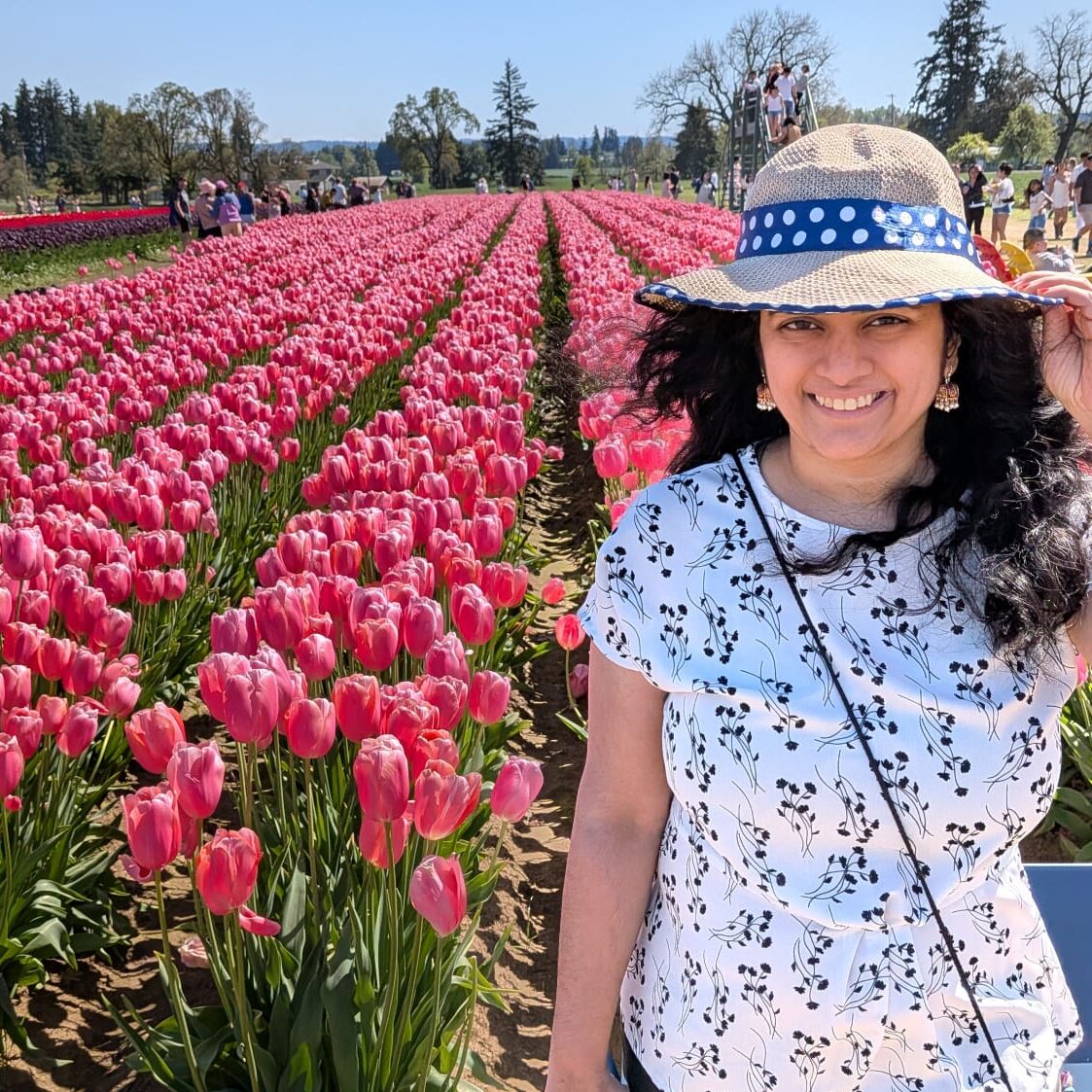 Woman with long dark hearing, wearing a hat, and standing in a field of tulips