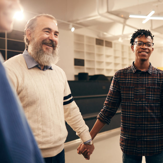 Group of happy people standing holding hands and smiling to each other during business training at office