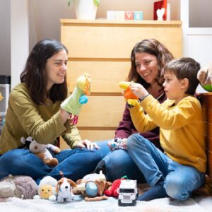A mom and her young child play with an Early Childhood Education Specialist during a home visit, with puppets on their hands.