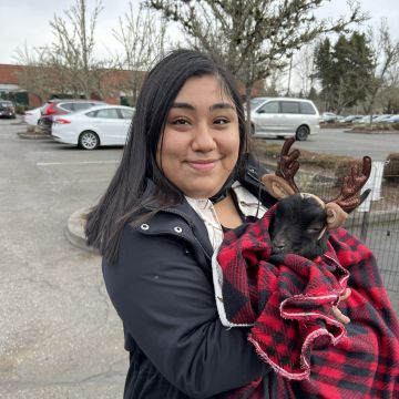 Luz stands in the LifeWorks NW parking lot, holding a therapy goat, smiling at the camera.