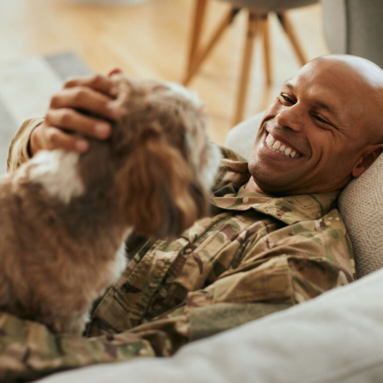 A man pets his dog happily while lying on a couch.