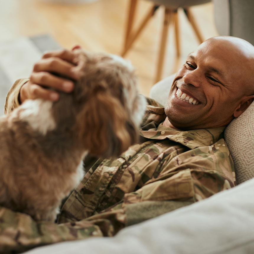A man pets his dog happily while lying on a couch.