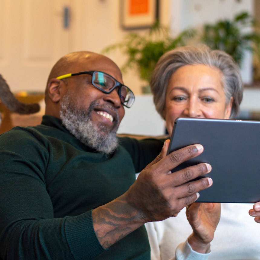 An older couple sits on a couch while looking at their estate planning documents on a tablet.