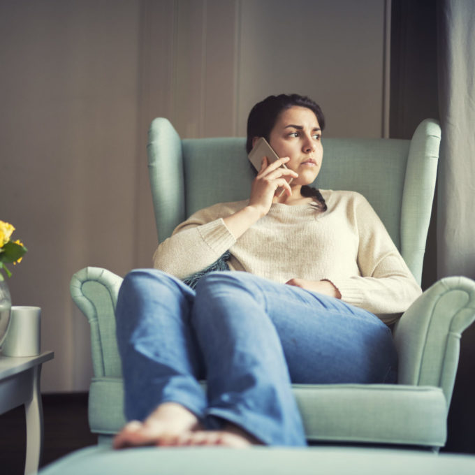 Woman speaks on the phone at home, she looking sad A young woman frowning as she speaks on the phone