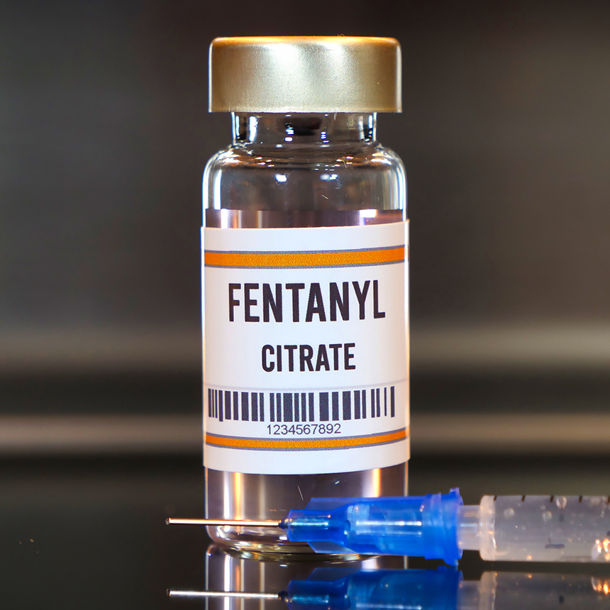 Fentanyl drug and syringe on black table with reflections and stainless background.