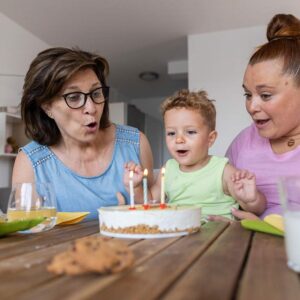 A mother, daughter, and granddaughter celebrate the youngest's birthday by blowing out candles on a cake.