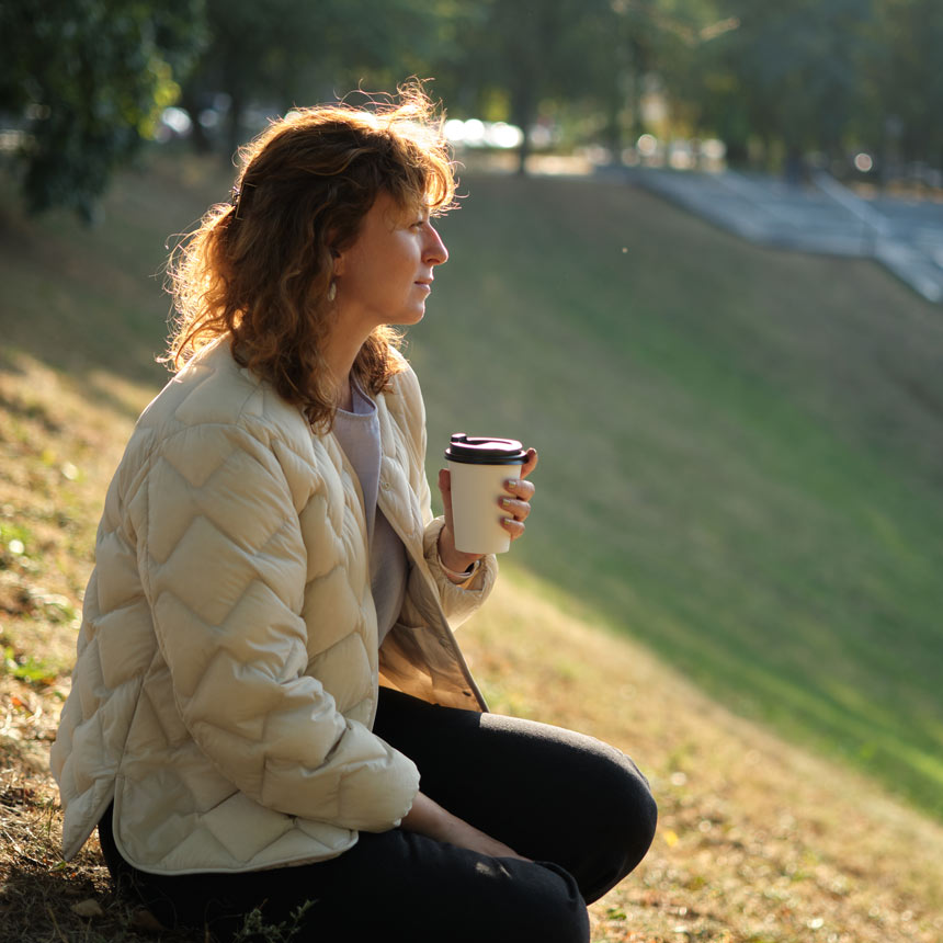 Woman with coffee outdoors in early morning.